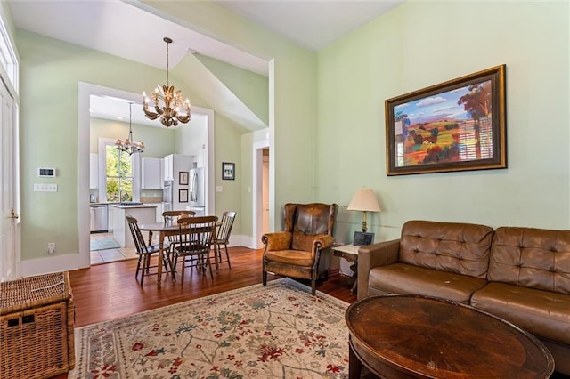 living room featuring light wood finished floors, an inviting chandelier, baseboards, and vaulted ceiling