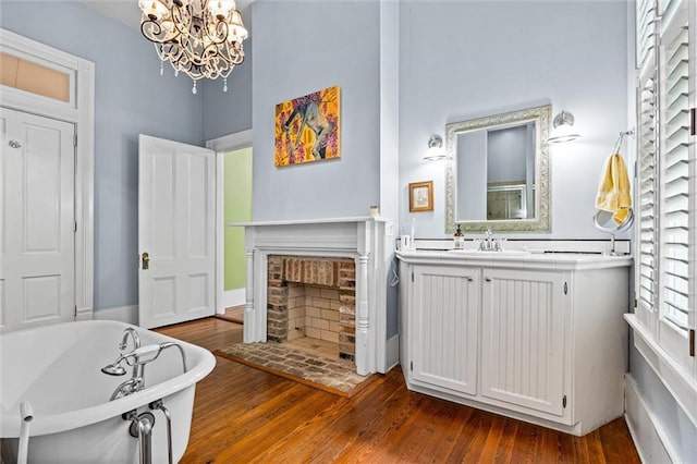 full bath with an inviting chandelier, a freestanding tub, vanity, wood finished floors, and a brick fireplace