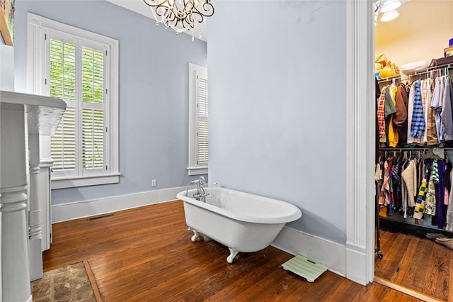 full bath featuring a notable chandelier, baseboards, visible vents, hardwood / wood-style floors, and a freestanding bath