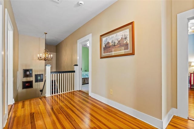 corridor featuring an upstairs landing, a notable chandelier, baseboards, and wood finished floors