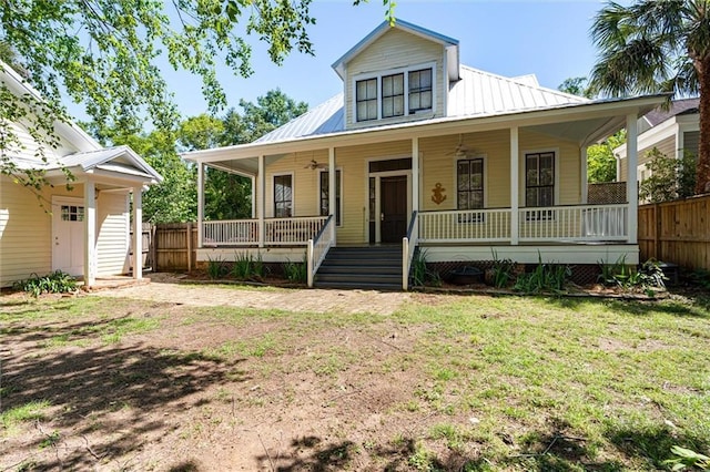 farmhouse featuring a porch, metal roof, fence, and a front lawn
