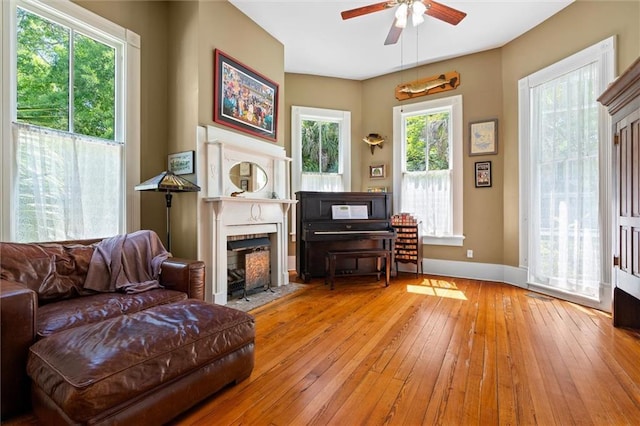 sitting room featuring a fireplace with flush hearth, wood-type flooring, baseboards, and ceiling fan