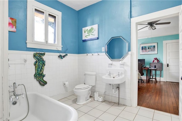 bathroom with ceiling fan, toilet, tile walls, tile patterned floors, and a tub