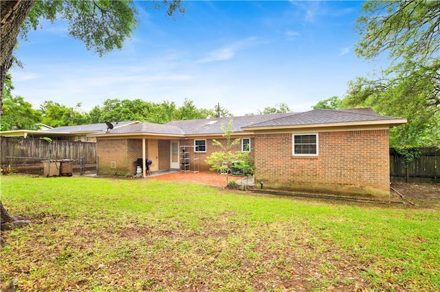 back of house featuring brick siding, a lawn, fence, and a patio area