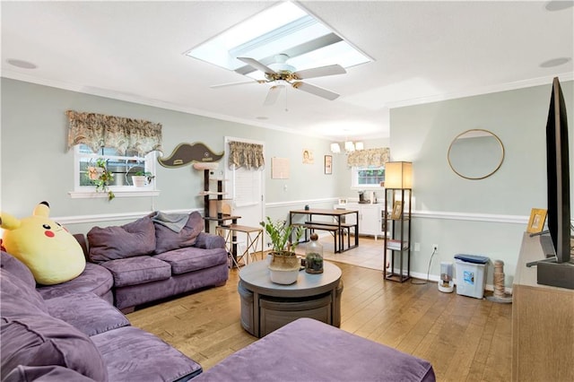 living room with a skylight, ornamental molding, ceiling fan with notable chandelier, and hardwood / wood-style floors