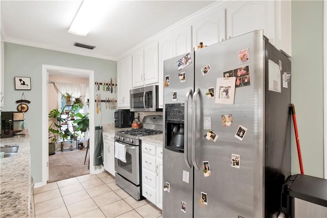 kitchen featuring light tile patterned floors, light stone counters, ornamental molding, stainless steel appliances, and white cabinetry