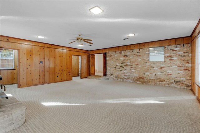 unfurnished room featuring light carpet, wood walls, ceiling fan, and brick wall