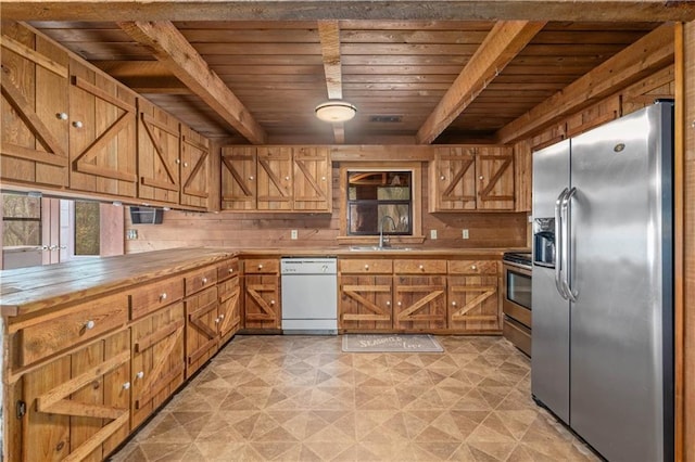 kitchen with beam ceiling, appliances with stainless steel finishes, sink, and wooden walls