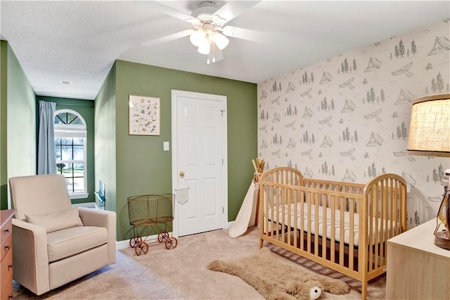 carpeted bedroom featuring a textured ceiling, a nursery area, and ceiling fan