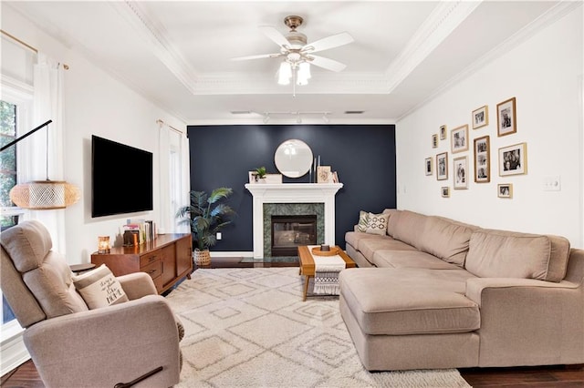 living room with hardwood / wood-style floors, ceiling fan, a raised ceiling, and a premium fireplace