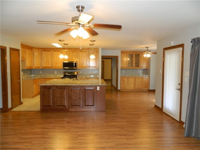 kitchen featuring light stone counters, tasteful backsplash, decorative light fixtures, stainless steel appliances, and light wood-type flooring