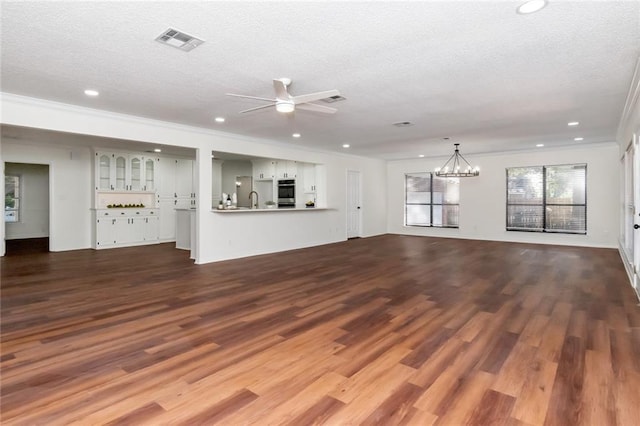 unfurnished living room with ceiling fan with notable chandelier, a textured ceiling, hardwood / wood-style flooring, and ornamental molding