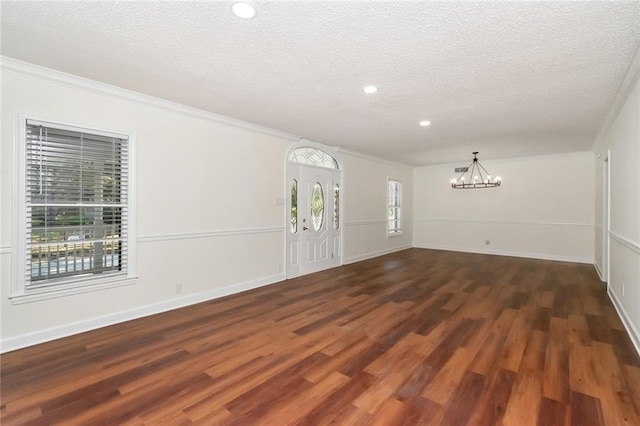 spare room featuring a textured ceiling, dark hardwood / wood-style flooring, ornamental molding, and a notable chandelier