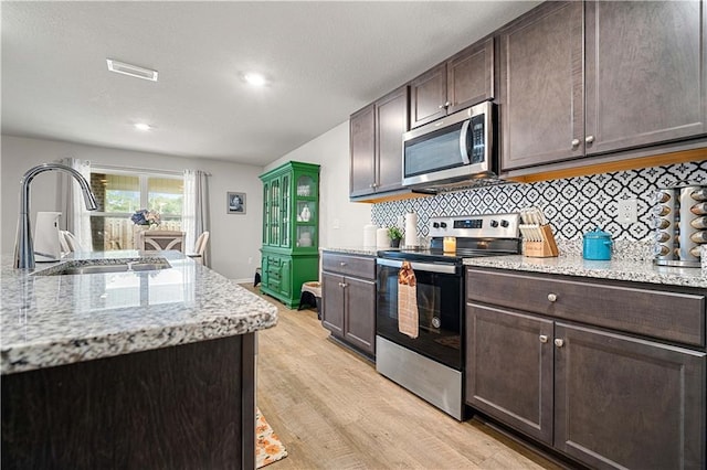 kitchen with light stone countertops, appliances with stainless steel finishes, sink, and dark brown cabinets