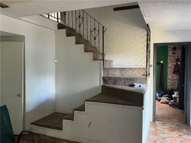 staircase featuring carpet flooring and a textured ceiling