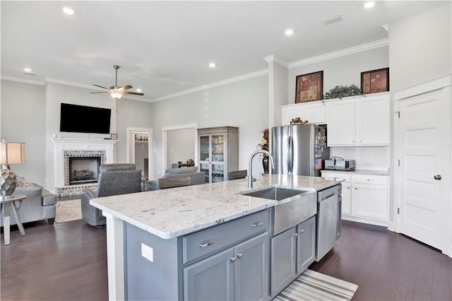 kitchen featuring appliances with stainless steel finishes, white cabinets, a fireplace, a center island with sink, and sink