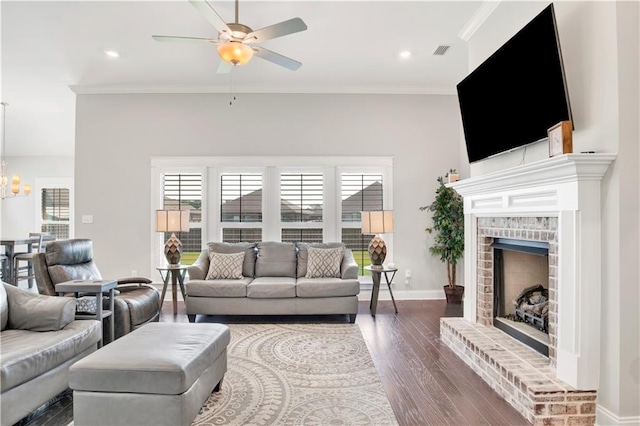 living room featuring ceiling fan with notable chandelier, a fireplace, ornamental molding, and dark wood-type flooring