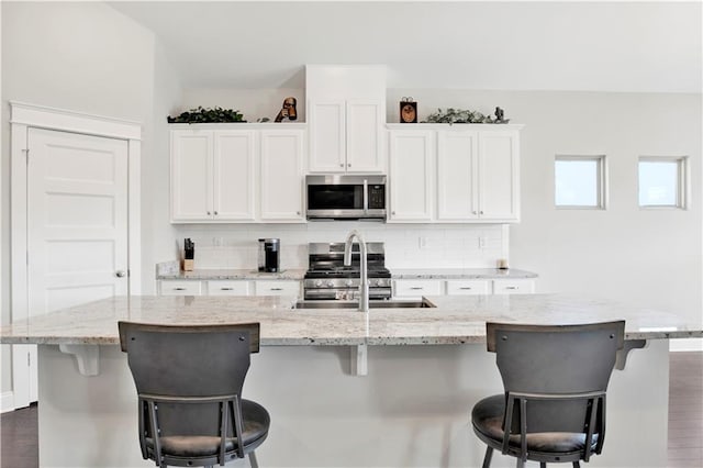 kitchen featuring a breakfast bar, stainless steel appliances, white cabinets, and a center island with sink