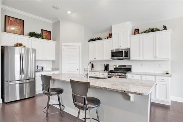 kitchen with white cabinets, a center island with sink, appliances with stainless steel finishes, and a breakfast bar area