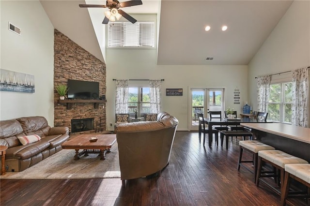 living room with dark hardwood / wood-style floors, a stone fireplace, ceiling fan, and high vaulted ceiling