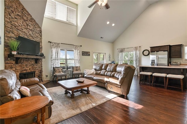 living room featuring high vaulted ceiling, a fireplace, ceiling fan, and dark wood-type flooring