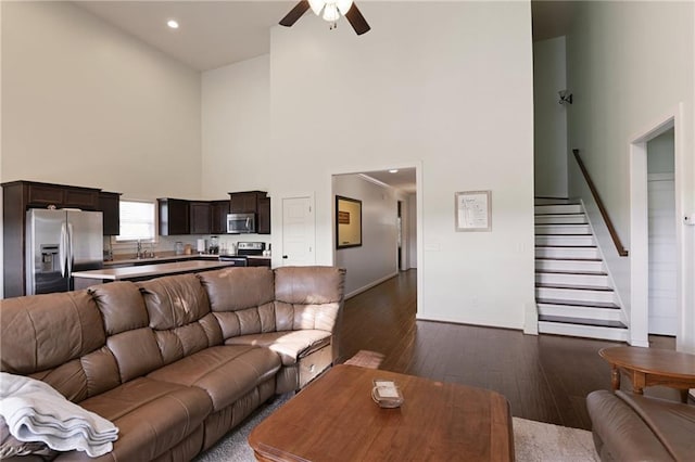 living room with dark wood-type flooring, ceiling fan, and a towering ceiling