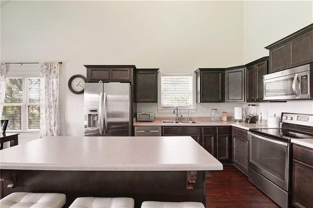 kitchen with dark hardwood / wood-style flooring, a kitchen bar, appliances with stainless steel finishes, dark brown cabinetry, and sink