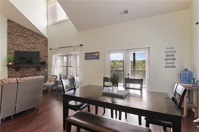 dining room with french doors, a stone fireplace, dark hardwood / wood-style floors, and a high ceiling