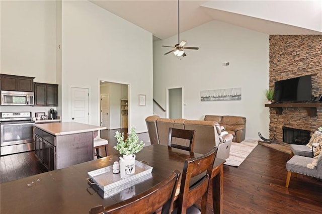 dining room featuring ceiling fan, a stone fireplace, high vaulted ceiling, and dark wood-type flooring