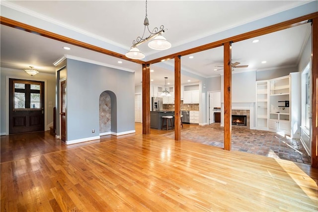 unfurnished living room featuring ceiling fan, hardwood / wood-style flooring, a fireplace, and ornamental molding