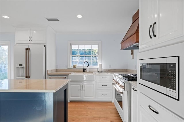 kitchen with white cabinets, custom exhaust hood, high end appliances, and light wood-type flooring