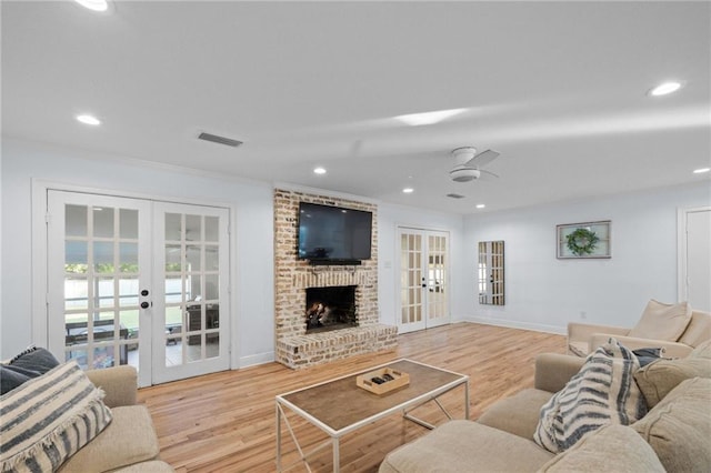 living room featuring french doors, crown molding, ceiling fan, light wood-type flooring, and a fireplace