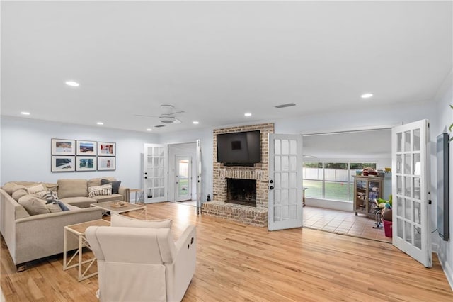 living room featuring french doors, light hardwood / wood-style floors, and a brick fireplace