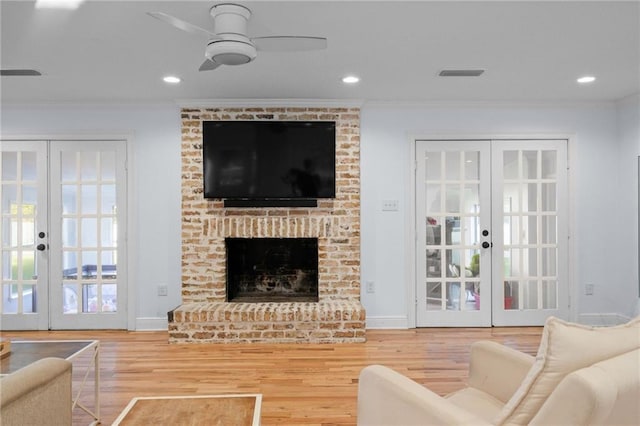 living room with french doors, a brick fireplace, crown molding, and wood-type flooring