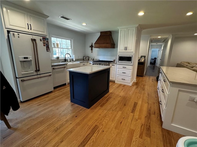 kitchen featuring custom exhaust hood, a center island, light hardwood / wood-style flooring, white cabinetry, and stainless steel appliances