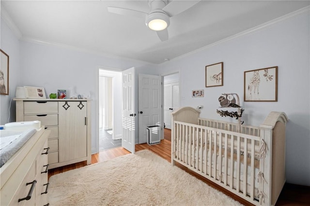 bedroom with ceiling fan, ornamental molding, a nursery area, and light hardwood / wood-style flooring