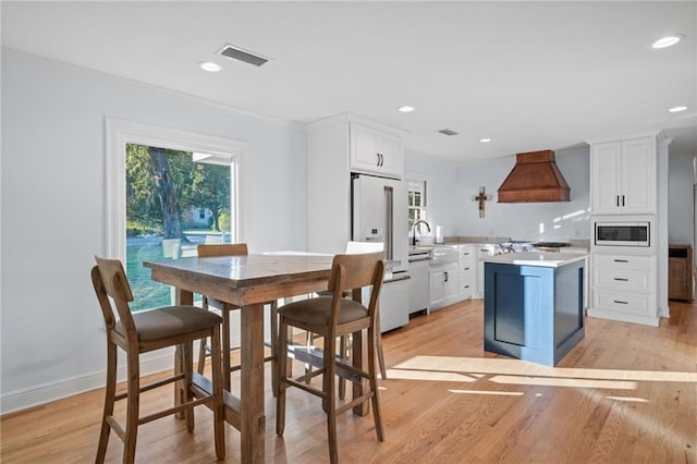 kitchen featuring premium range hood, white appliances, a kitchen island, light hardwood / wood-style flooring, and white cabinetry