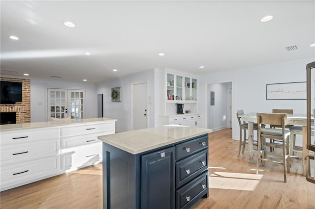 kitchen featuring a fireplace, light wood-type flooring, white cabinetry, and a kitchen island