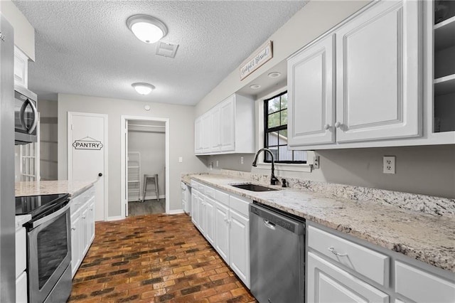 kitchen featuring white cabinets, sink, light stone countertops, a textured ceiling, and stainless steel appliances