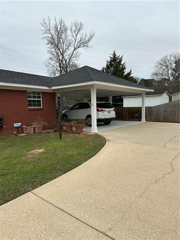 view of parking with a carport, driveway, and fence