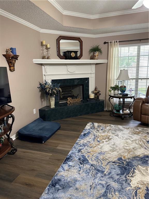 living area featuring a ceiling fan, a tile fireplace, ornamental molding, wood finished floors, and a textured ceiling