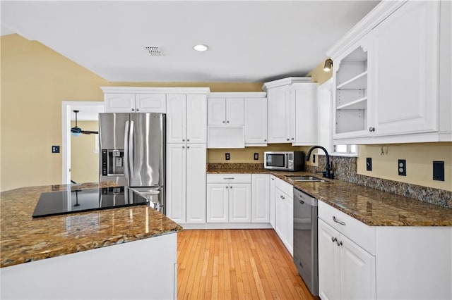 kitchen featuring appliances with stainless steel finishes, white cabinets, a sink, dark stone counters, and light wood-type flooring