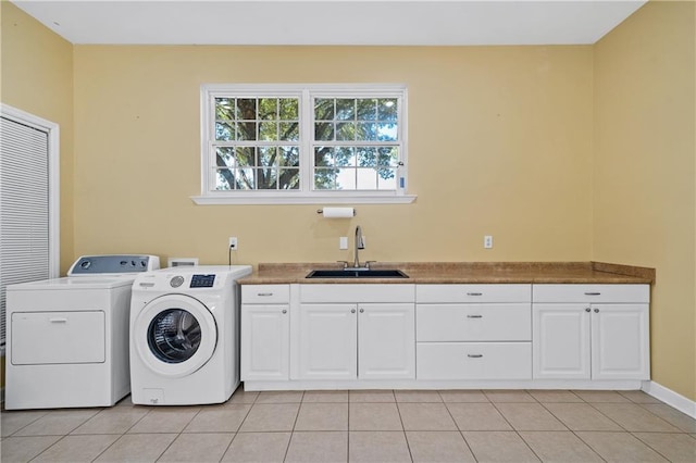 clothes washing area with washing machine and clothes dryer, light tile patterned floors, cabinet space, a sink, and baseboards