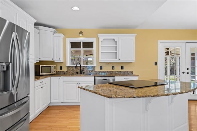 kitchen with white cabinets, appliances with stainless steel finishes, a center island, a kitchen bar, and a sink