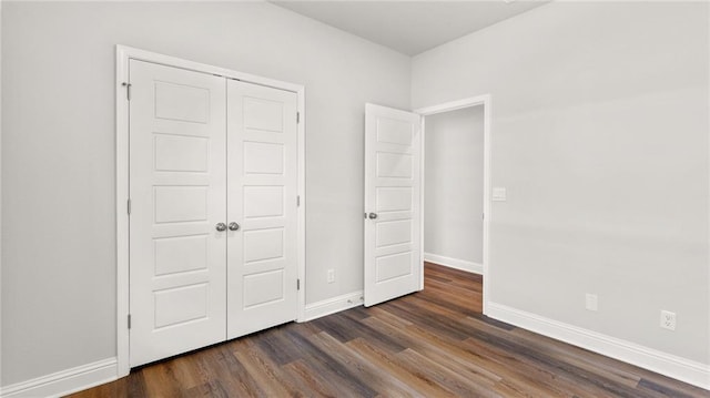 unfurnished bedroom with baseboards, a closet, and dark wood finished floors