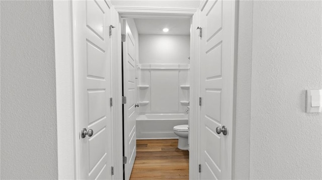 full bathroom with a textured wall, toilet, and wood finished floors