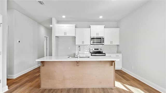 kitchen with visible vents, an island with sink, a sink, light wood-style flooring, and appliances with stainless steel finishes