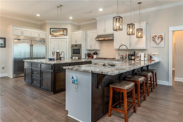 kitchen with backsplash, dark wood-type flooring, stainless steel built in fridge, white cabinetry, and under cabinet range hood