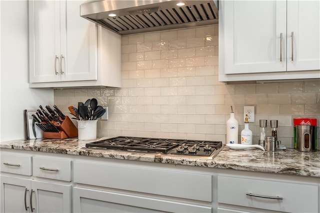 kitchen featuring wall chimney exhaust hood, stainless steel gas stovetop, white cabinetry, and decorative backsplash