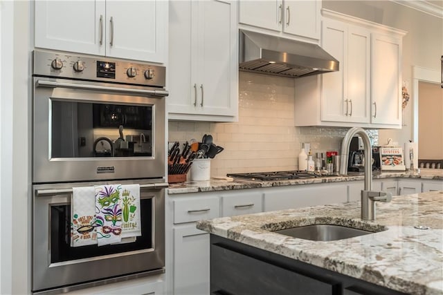 kitchen featuring double oven, under cabinet range hood, a sink, white cabinets, and backsplash